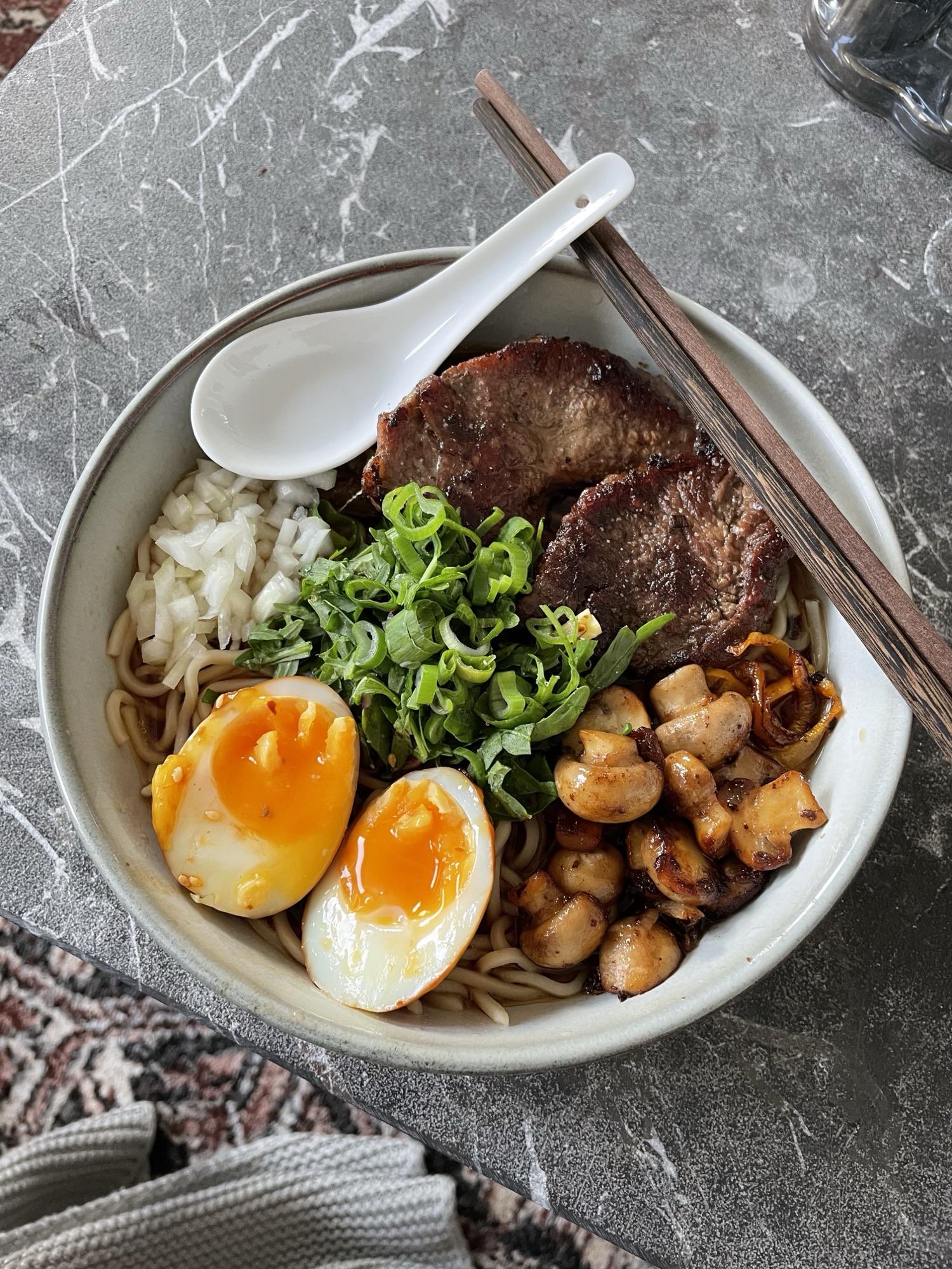 Top-down bowl of ramen with steak, soft eggs, mushrooms and spring onion